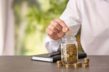 Man putting coin into glass jar on table