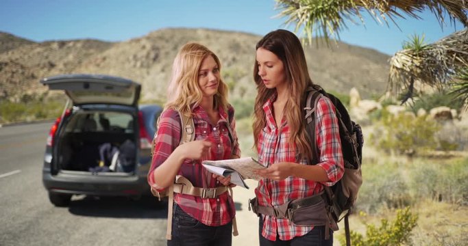 Portrait of two adventurous young ladies looking at a map in a desert setting outdoors, Two attractive white female hikers deciding where to go for their hike in the desert, 4k