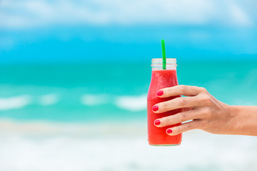 Hand holding refreshing strawberry, watermelon smoothie on the beach. 