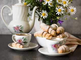Croissants (bagels) with poppy seeds and tea on a bouquet of flowers field background. Morning tea with croissants.