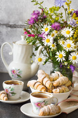 Croissants (bagels) with poppy seeds and tea on a bouquet of flowers field background. Morning tea with croissants.