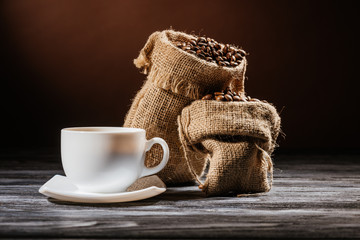 close-up shot of cup with sacks of coffee on rustic wooden table