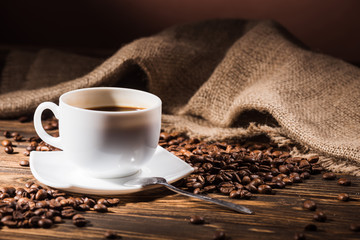 cup of coffee with roasted beans and sackcloth on wooden table