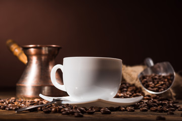 close-up shot of cup of coffee with roasted beans and vintage cezve on dark brown background