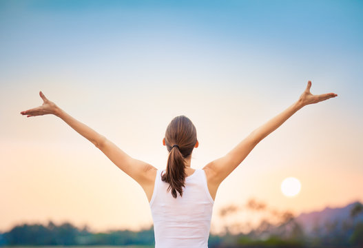 Young woman raising her arms up against the sunset feeling free.  Happiness and joy concept. 
