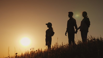 Silhouettes of a happy family, together they meet the dawn in a picturesque place
