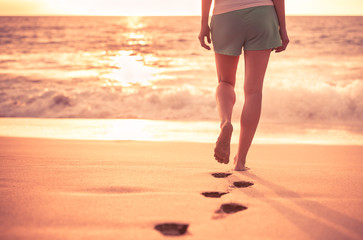 Woman walking on a beautiful tropical beach leaving foot prints in the sand. 