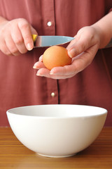Female hands smash the chicken egg with a knife over a bowl of wheat flour in the kitchen
