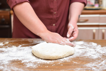 Women's hands knead the dough in the kitchen on the table. Close-up