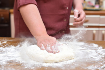 Women's hands knead the dough in the kitchen on the table. Close-up