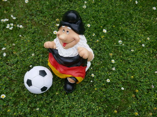 Lustiger Gartenzwerg, ein Fußballfan mit einer Deutschlandfahne und einem Fußball, sitzt auf...