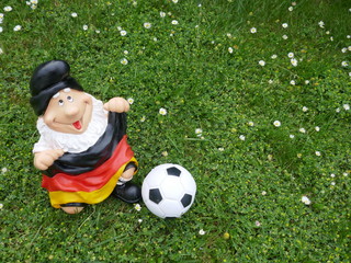 Lustiger Gartenzwerg, ein Fußballfan mit einer Deutschlandfahne und einem Fußball, sitzt jubelnd ...