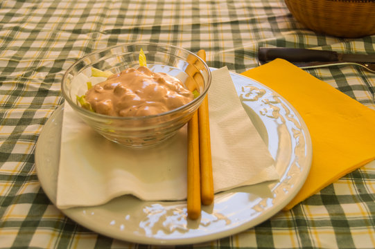 Shrimp cocktail in a glass bowl with breadsticks own on an orange napkin on a white plate