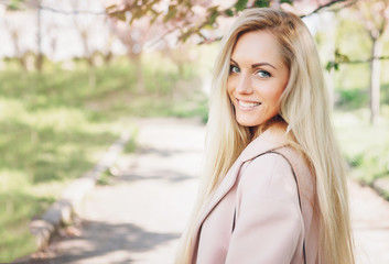 Naklejka premium Woman with long blond hair in the garden with flowers. Beautiful girl on a sunny day.