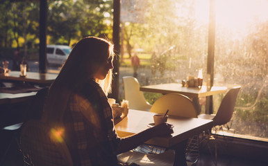 Young female student sitting in modern coffe shop. Sunset.Woman sitting in front of the window in ...