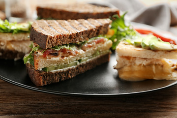 Plate with delicious sandwiches on wooden table