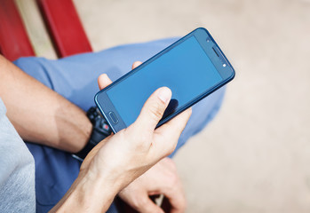 the man is sitting on a bench and using a smartphone with a gray display on the city street, close-up Blank screen for graphics display montage.