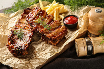 Delicious grilled ribs with sauce and french fries on parchment