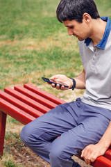 Obraz premium the man is sitting on a bench and using a smartphone with a gray display on the city street, close-up