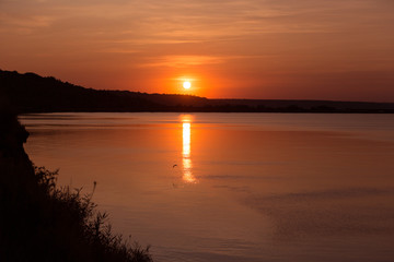 Obraz premium orange sunset, reflection in water, birds over a pond, coastline, concept summer and nature