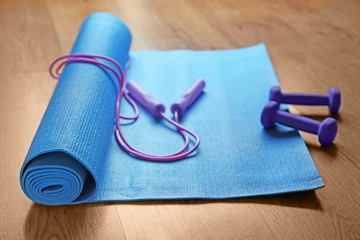 Yoga mat with jumping rope and dumbbells on wooden floor