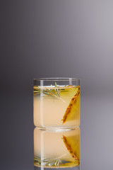glass of fresh pineapple cocktail on reflective surface and on grey