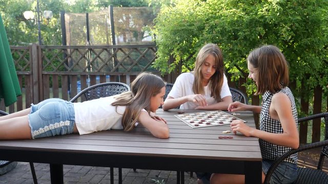 Playing checkers sitting at terrace table teenager sisters girls triple twins have fun together