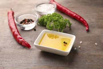 Bowl of fresh olive oil with chili and spices on wooden table