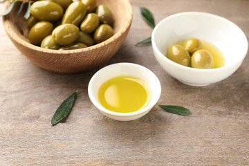 Bowls with oil and olives on wooden table