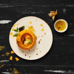 Delicious vegetable soup decorated with basil leaves and cooked in pumpkin lying on flat round plate standing on blue aged wooden surface. Tasty restaurant vegetarian meal, veggie recipe. Top view.