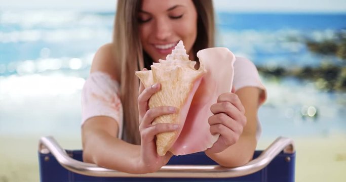Close-up of conch shell being held by woman out of focus in background at beach, Seashell in hands of smiling pretty girl on vacation in serene beach setting, 4k