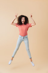 Pretty young woman jumping showing peace gesture.