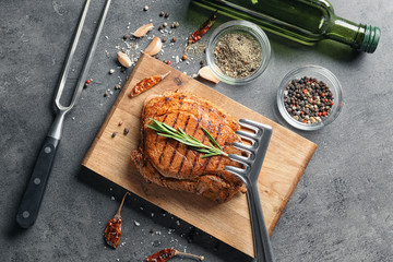 Wooden board with tasty grilled steak and spices on grey background