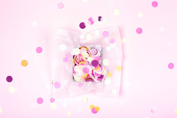 One box with colorful confetti on pink background. Festive card. Top view.