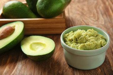 Bowl with tasty guacamole and ripe avocados on wooden table