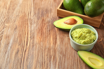 Bowl with tasty guacamole and ripe avocados on wooden table