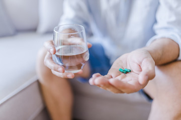 Young man with pill and glass of water at home, closeup