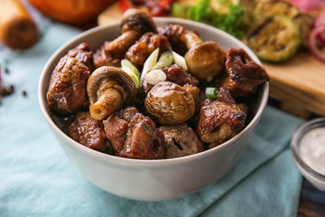 Bowl with pieces of shish-kebab and mushrooms on table