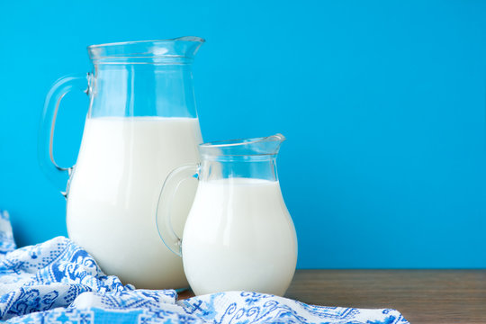 Jugs of milk on a blue background. Two glass jug of milk and a kitchen towel on a blue background.