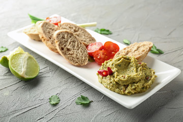 Plate with delicious guacamole on plate and sliced bread on grey textured background