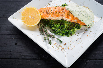 Delicious fish steak with sauce and herbs on wooden background
