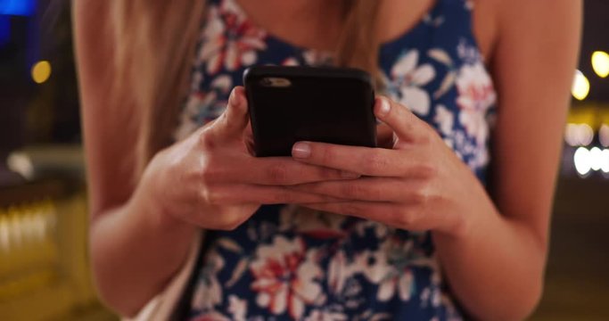 Extreme close-up of young womans hands texting with phone in in city street, Millennial in romper using smartphone app in tight close-up outdoors at night, 4k