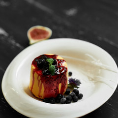 Delicious cake served with blueberries, jam and mint leaves on round plate, fig and cornflowers lying on blue aged wooden surface. Tasty gourmet berry dessert, appetizing sweet meal. Top view.