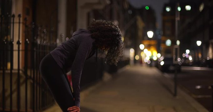 Black woman athlete in the city at night taking a break from jog, Female jogger in active wear on city street taking a breath, 4k