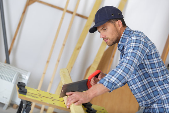 handyman cutting wood with hand saw in the garage