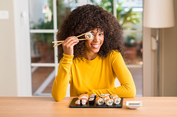 African american woman eating sushi using chopsticks at home with a happy face standing and smiling with a confident smile showing teeth