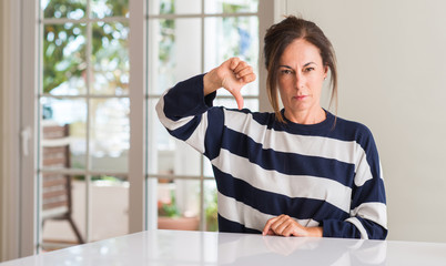 Middle aged woman with angry face, negative sign showing dislike with thumbs down, rejection concept