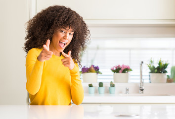 African american woman wearing yellow sweater at kitchen pointing fingers to camera with happy and funny face. Good energy and vibes.