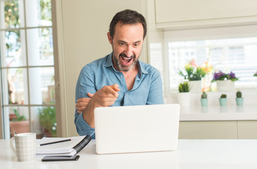 Middle age man using laptop at home very happy pointing with hand and finger to the side