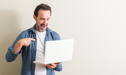 Senior man using laptop computer with surprise face pointing finger to himself